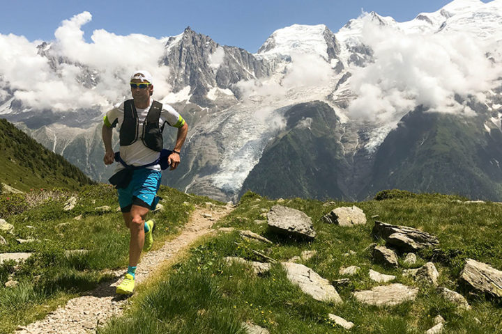 A man wearing sportswear and sunglasses is running along a path in the mountains.
