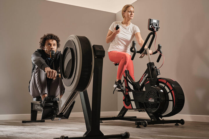 man indoor rowing using POWERbreathe IMT device and lady on spin bike