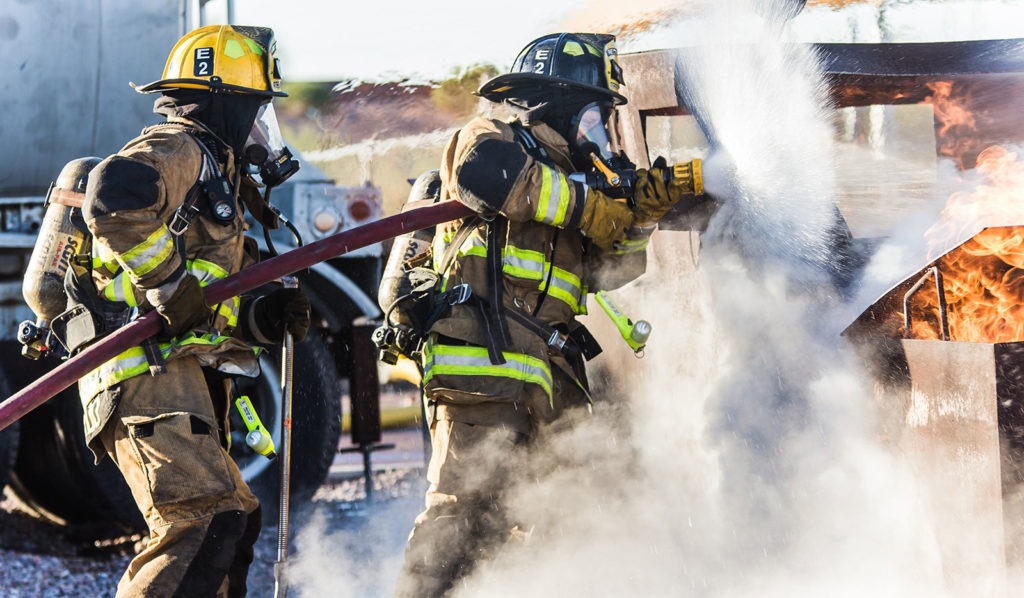 Two firefighters are using a hose to extinguish a fire.