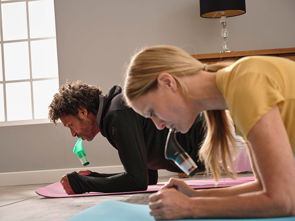 A man and woman are in the plank position whilst using a POWERbreathe device.