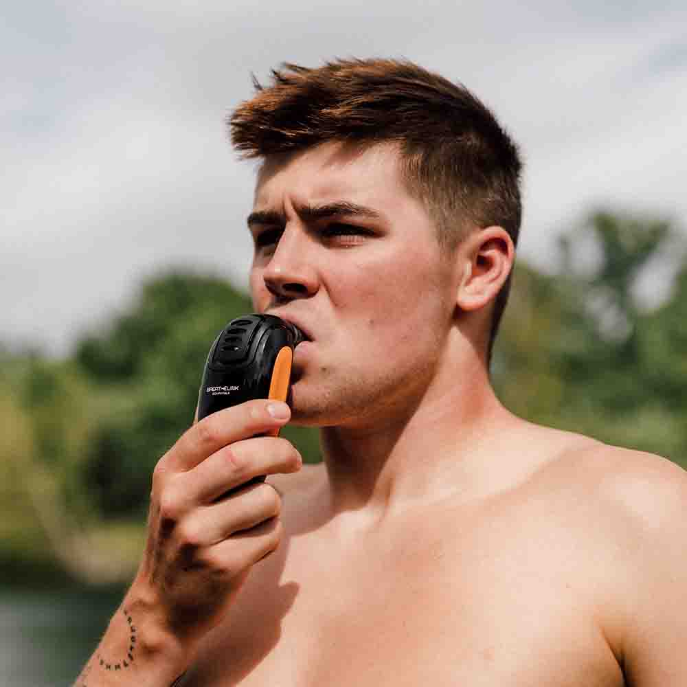 Close up of a man next to a lake has a POWERbreathe Plus with Smart Adaptor in his mouth.