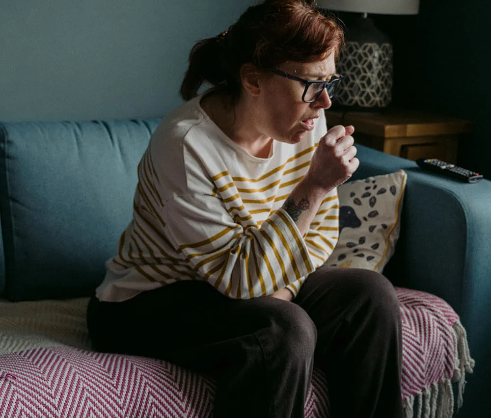 A lady sat on a sofa coughing