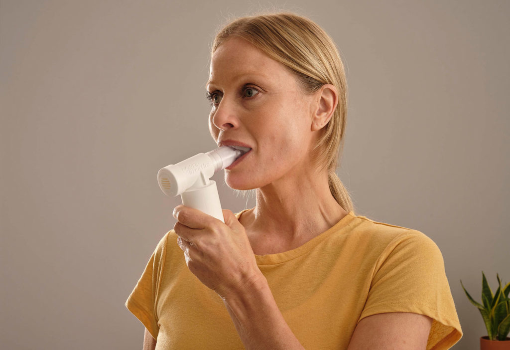 a woman using powerbreathe breathing trainer medic