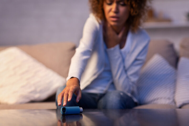 person sitting on sofa reaching for asthma inhaler