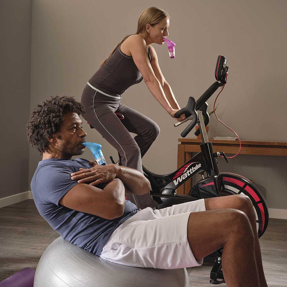 A man leaning back on a balance ball with a Blue Plus in his mouth and a woman on a Wattbike with a Red Plus in her mouth.